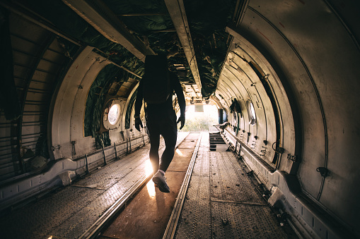 Handsome and athletic man with a bag on his back, standing in a abandoned airplane.