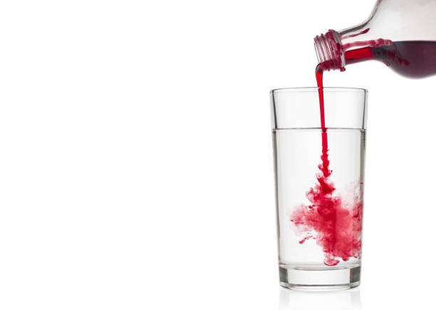 istock Cranberry syrup pouring into water glass on white background 1044955608