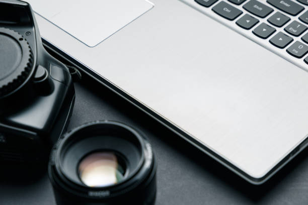 istock Work space on black table of photographer. Minimal workspace with Laptop, camera and lens copy space on dark background. Modern and elegant. Close up. 1044969192