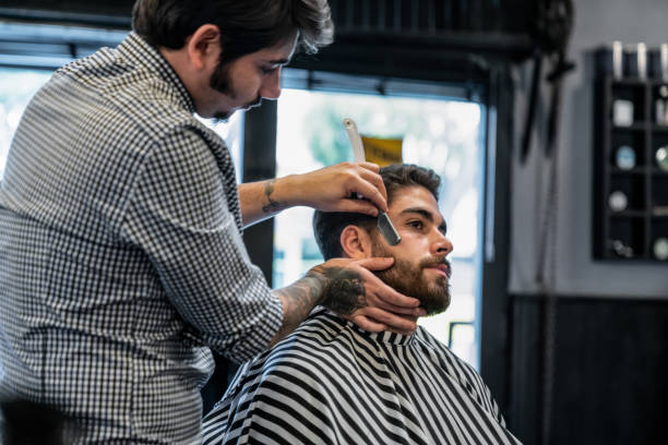 istock Young barber shaving a customers beards with a retro style razor 1044971516