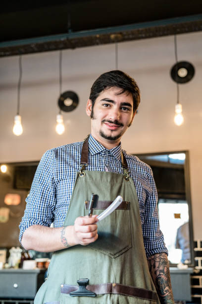 istock Latin american young barber holding a shaving knife while looking at camera smiling 1044971544