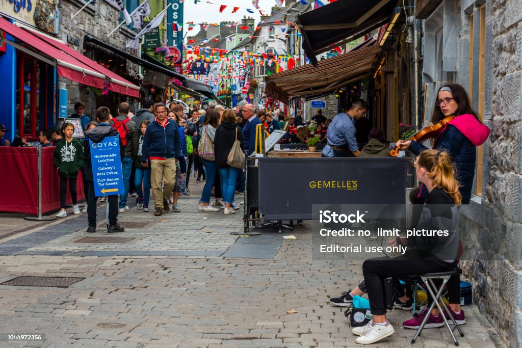 street musician performing in streets of Galway Galway, Ireland - August 07, 2018: People walking along one of the main pedestrian streets in Galway. It is full of shops, pubs and restaurants. Street musicians are performing. Ireland Stock Photo