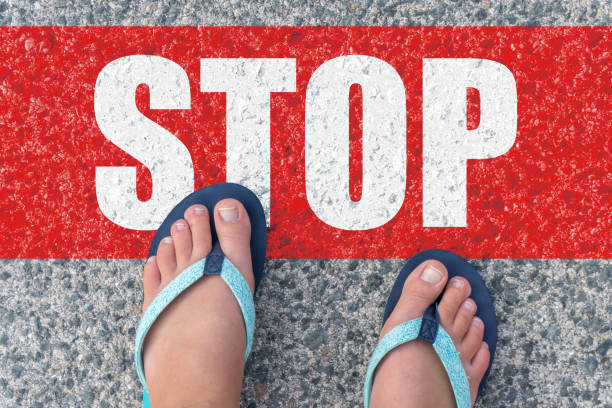 istock View from above, female feet with text stop written on grey sidewalk. 1044996848