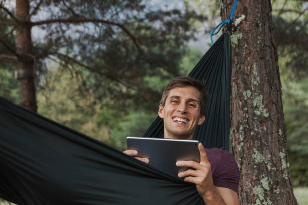 istock young man smiling to camera and using a tablet on a hammock 1044997692