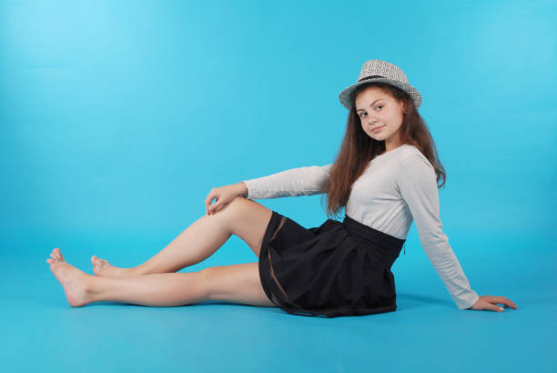 Young girl sitting on floor against blue background in studio.