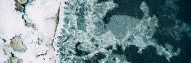 istock Ice fragments under thin layer of frozen river water. Dark blue natural background 1045003220