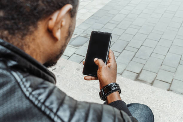istock Dark-skinned man looking at mobile phone screen and sitting on concrete steps. 1045008574
