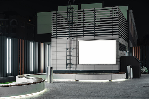 Blank white outdoor banner at bright modern building wall at night time, mock up. 3d rendering.