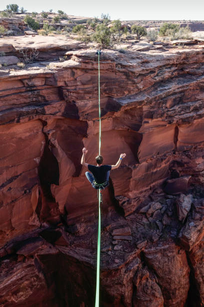 Man catching balance on the slackline - highline Slackliner catching balance on high-line between cliffs in Utah. highlining stock pictures, royalty-free photos & images