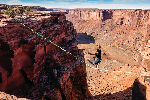 Slackliner is hanging on high-line between cliffs in Utah.