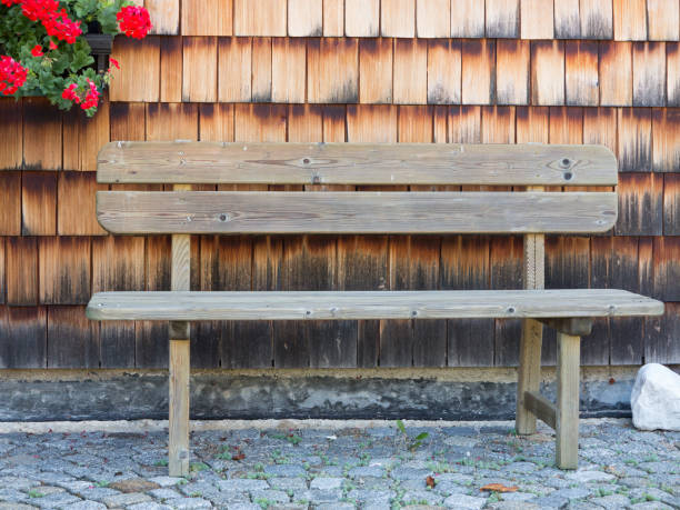 istock Wooden bench on cobblestone pavement against wooden wall 1045018468