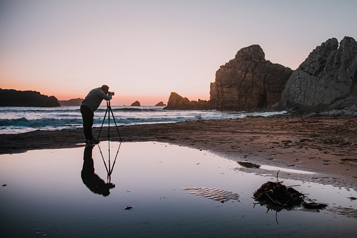 Photographer with tripod at sunset and his reflection on the water