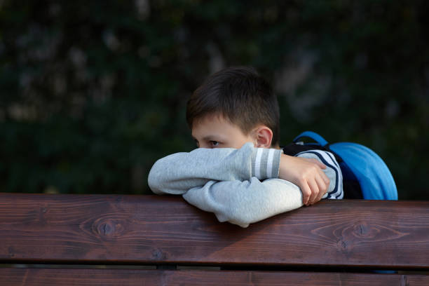 Schoolboy sits on a bench at a school park and cries. Negative emotion.