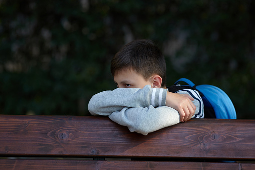 Schoolboy sits on a bench at a school park and cries. Negative emotion.