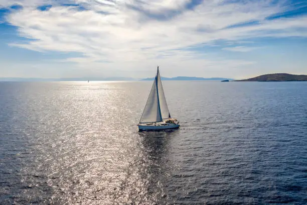 Aerial view of a sailingboat on the blue, mediterranean sea against the sparkling sunlight