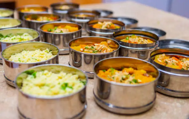 Photo of Rows of Tiffin (Dabba) Meal Box Containers Filled with Herbed Couscous and Vegetable Stew