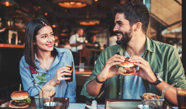 朝食を食べて、カフェに座って美しい若いカップル。愛、出会い系、食品、ライフ スタイルのコンセプト - burger hamburger food fast food ストックフォトと画像