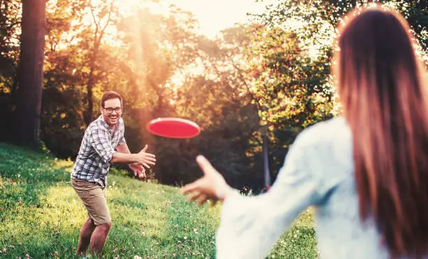 Young couple playing frisbee in the park and enjoying in moments of happiness. Sport, recreation, lifestyle, love concept