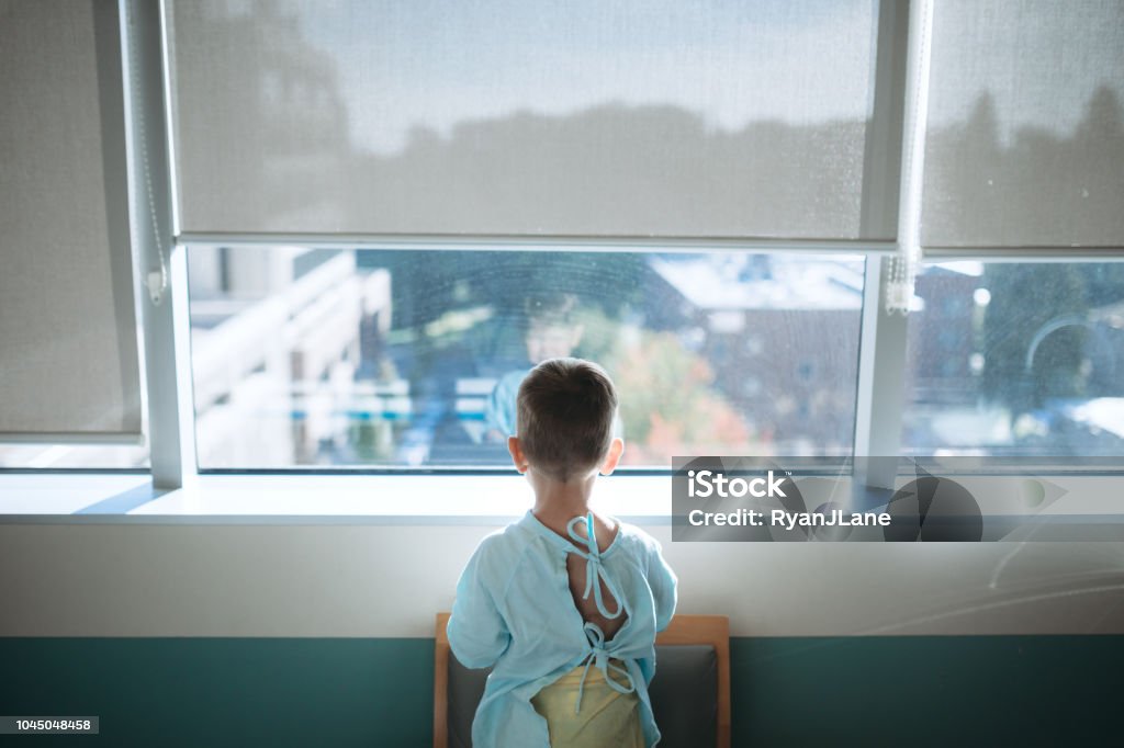 Toddler At Children's Hospital for Surgery A cute little Caucasian boy waits in the childrens hospital ward to be taken back for surgery.  He looks out of the window of his room while waiting for the doctor to arrive. Child Stock Photo