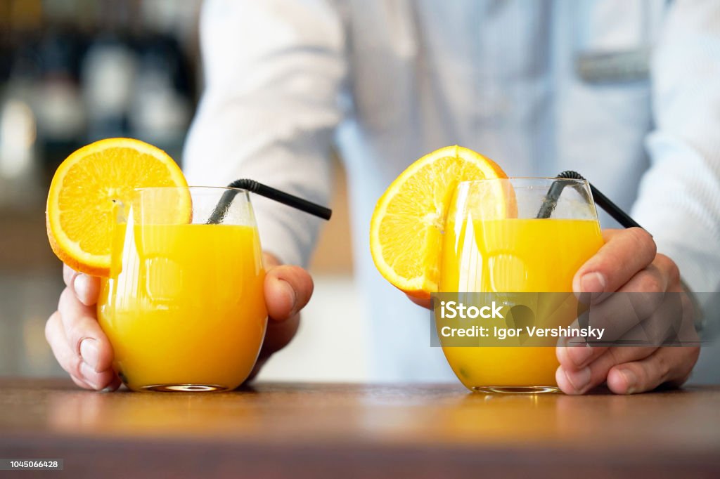 Two glasses of orange juice The barman gives two glasses of orange juice to the client of the hotel restaurant. The waiter transfers the order for two orange juice to the client of the hotel bar. The concept of service. Orange Juice Stock Photo