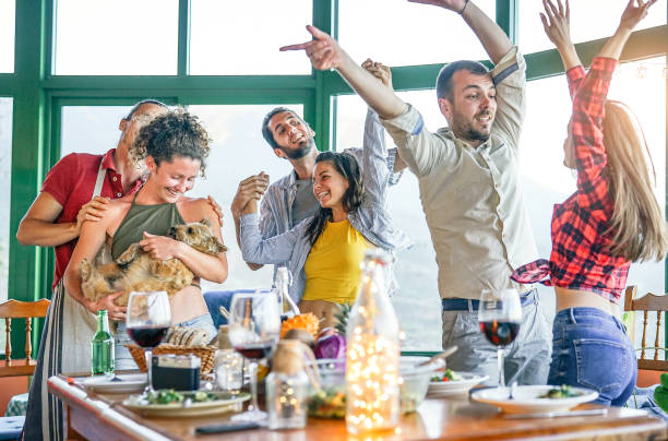 Happy friends dancing while making a vegetarian dinner in terrace - Young people having fun dining together in vineyard house  - Friendship and youth lifestyle concept