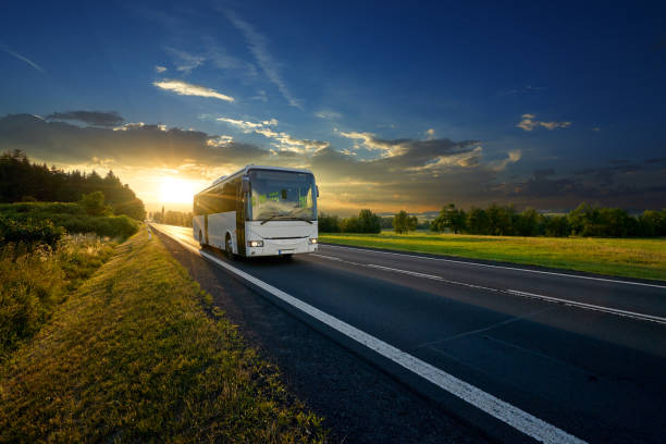 bus blanco que llega a la carretera de asfalto en un paisaje rural en los rayos de la puesta del sol - autobús fotografías e imágenes de stock