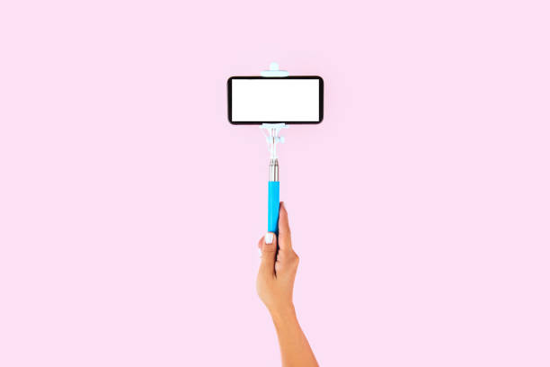 Selfie stick and white smart phone on pink background