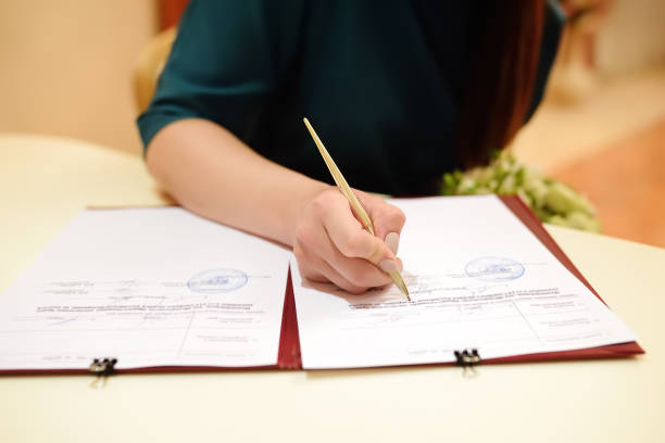 Bride signing the marriage certificate, with colored background and silver pen, you can see some pink candles.