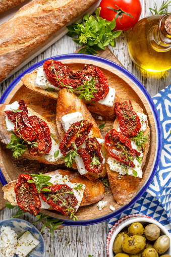 Bruschetta with feta cheese, dried tomatoes, olive oil and fresh aromatic herbs, on a plate on a wooden table. Delicious Mediterranean vegetarian appetizer