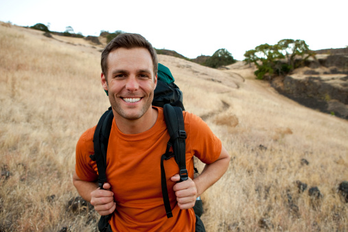 Man with a backpack smiling while standing on a trail when out hiking.