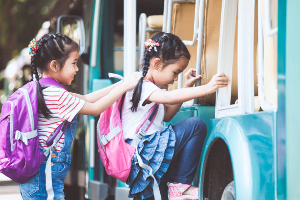 Asian pupil kids with backpack holding hand and going to school with school bus together stock photo