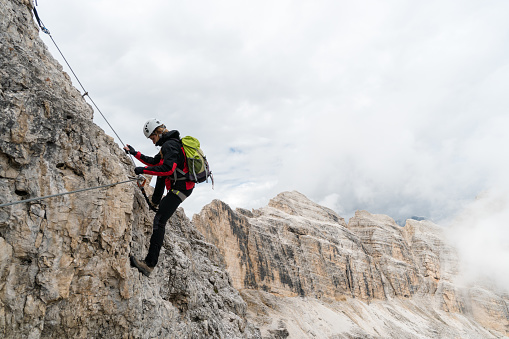 young attractive female university student on a steep and exposed rock face climbs a Via Ferrata in Alta Badia in the South Tyrol