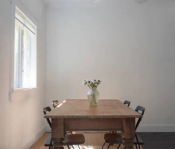 Photo of Wooden dining table with chairs and vase next to window
