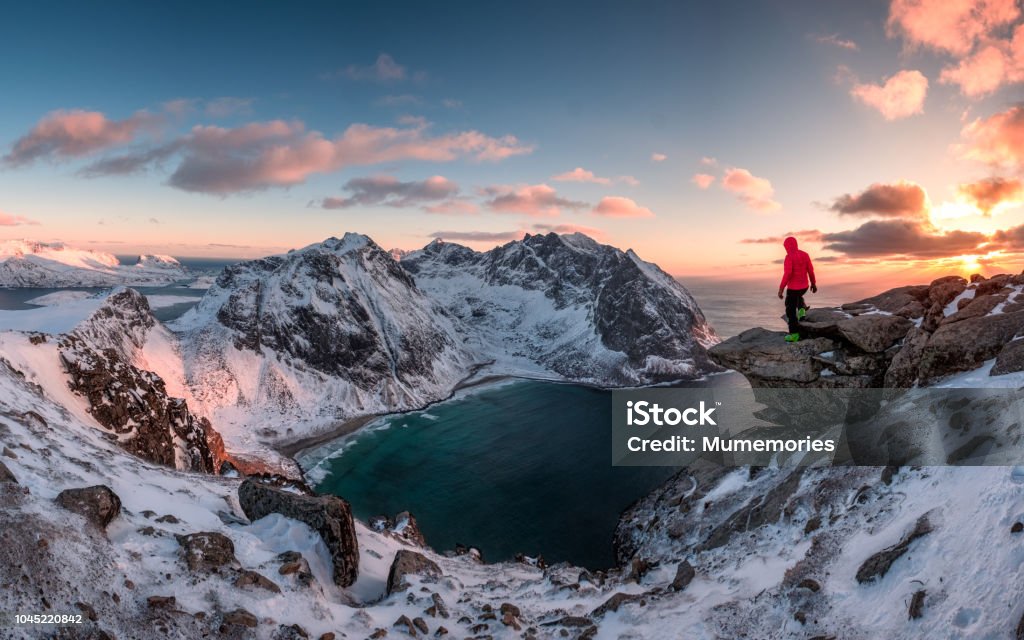 Man mountaineer standing on rock of peak mountain at sunset Man mountaineer standing on rock of peak mountain at sunset. Ryten Mountain, Norway Winter Stock Photo