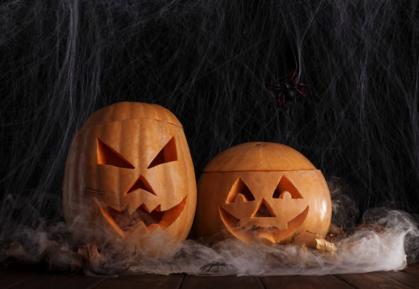 istock Two halloween pumpkins in spiderweb with spiders and autumn leaves 1045235564