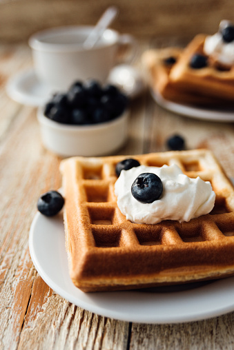 Brussels waffles with blueberry and whipped cream on wooden table at morning breakfast