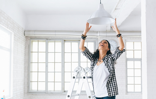 Woman hanging a lamp in new home Property Services. New Home.