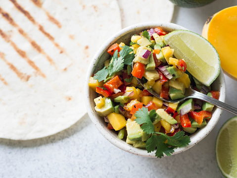 Salsa with mango, cilantro, onions and peppers close up in a bowl, tortillas grill  and ingredients on the table.