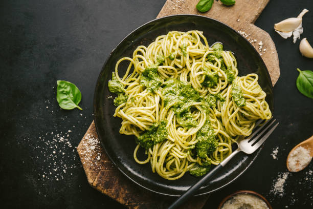 Tasty pasta with pesto served on plate Tasty appetizing pasta spaghetti with fresh sauce pesto and cheese served on plate on black table. View from above. Ready to eat. Horizontal noodles stock pictures, royalty-free photos & images