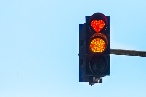 Traffic light with a red heart-shaped signal against a blue sky