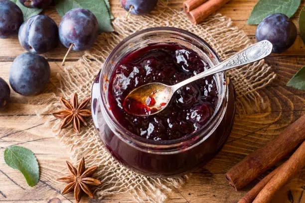 Plum jam in a glass jar. Fresh plum fruit on a wooden table.