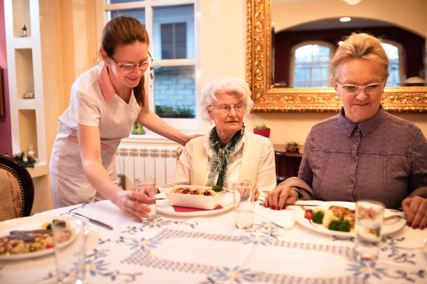 istock Careful nurse sets a table for dinner to patients at nursing home 1045299068