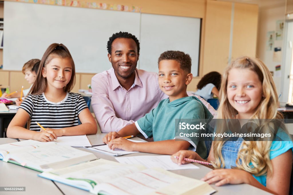 Insegnante di scuola maschile e bambini in classe sorridenti alla macchina fotografica - Foto stock royalty-free di Insegnante