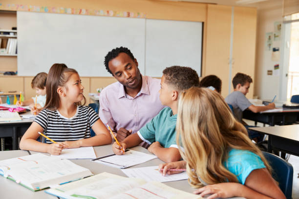 insegnante che lavora con i bambini delle scuole elementari alla loro scrivania - multi ethnic group concentration student asian ethnicity foto e immagini stock