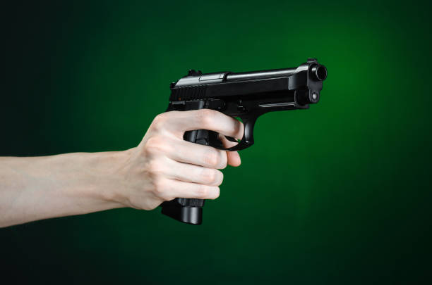istock Firearms and murderer topic: human hand holding a gun on a dark green background isolated in studio 1045323184