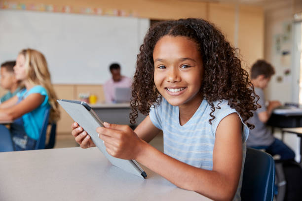 ragazza che usa il tablet a lezione di scuola sorridendo alla fotocamera da vicino - school age girl foto e immagini stock