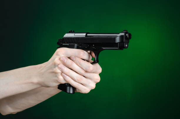 istock Firearms and murderer topic: human hand holding a gun on a dark green background isolated in studio 1045323210