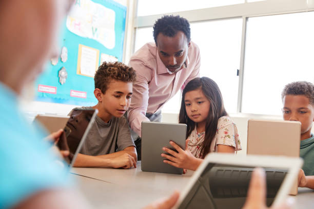 teacher among school kids using computers in class - multi ethnic group concentration student asian ethnicity imagens e fotografias de stock