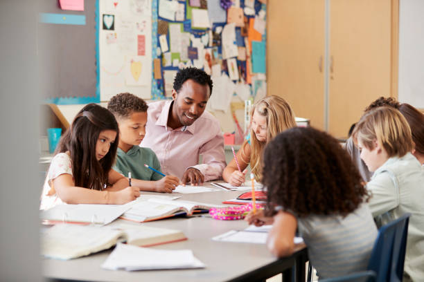 istock Male teacher works with elementary school kids at their desk 1045328024