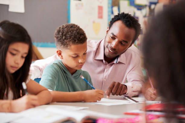 enseignant de sexe masculin travaillant avec le garçon de l’école primaire à son bureau - teacher child student education photos et images de collection